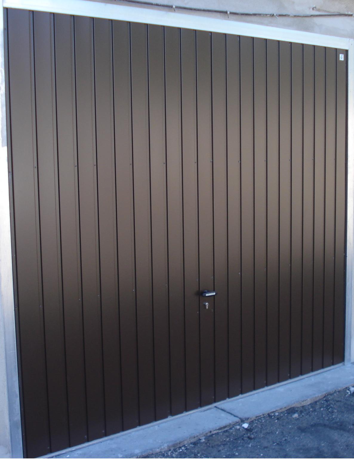 Zamknięta, brązowa brama garażowa segmentowa z pionowymi przetłoczeniami i srebrną ramą, widoczny zamek z kluczem.